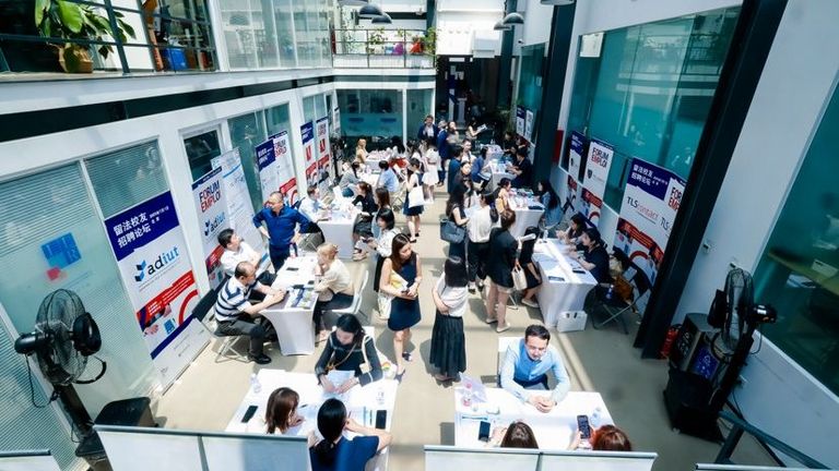 Hr event: People gathered in a modern office atrium featuring multiple floors, large glass windows, open walkways, and abundant natural light, creating a dynamic and collaborative business environment.
