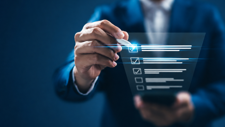Business professional interacting with a digital checklist on a transparent virtual interface. A hand holding a stylus marks completed tasks on a glowing blue checklist, symbolizing project management, quality control, compliance, workflow optimization, and digital transformation in a modern business environment.