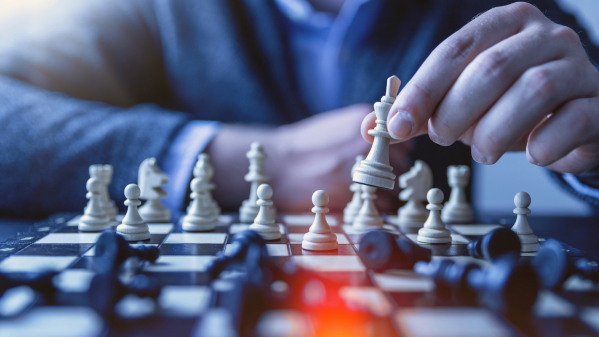 Person moving chess pieces on a chessboard, symbolizing strategic thinking, business planning, and decision-making.