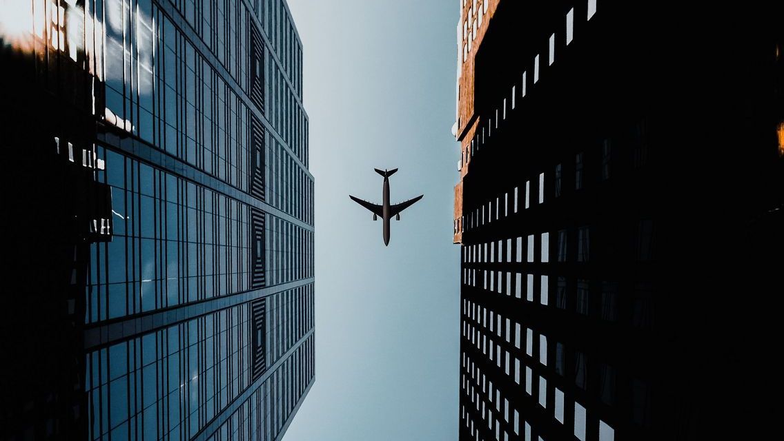 A commercial airplane flying directly between two modern glass skyscrapers.